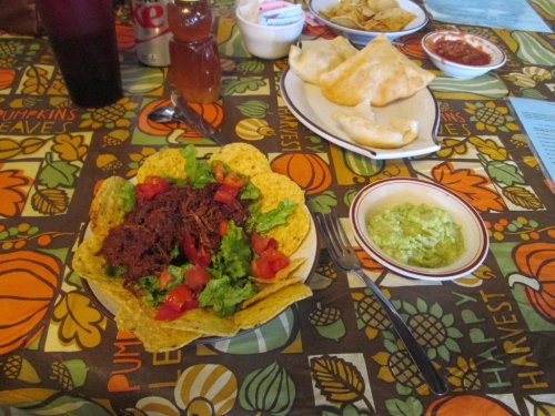 A colorful table setting with a taco salad, guacamole, and chips, surrounded by festive autumn-themed decor.