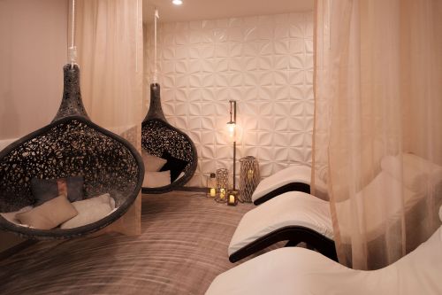 A serene relaxation area featuring hanging chairs, lounge chairs, soft lighting, and decorative elements.