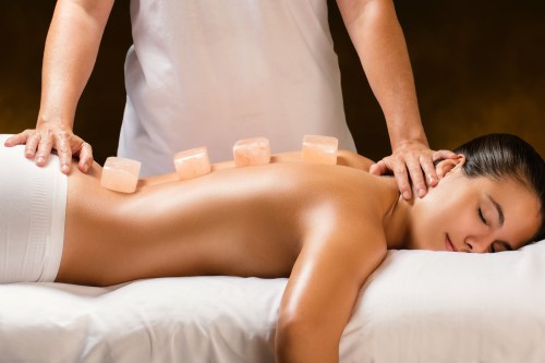 A woman receiving a massage with salt stones on her back, while a therapist applies pressure to her shoulders.