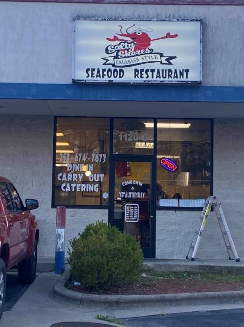 Exterior of a seafood restaurant with a sign that reads "Salty Sisters" and details for dining, carryout, and catering.