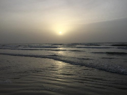 A serene beach at sunset, with gentle waves reflecting the soft light of the sun in a hazy sky.