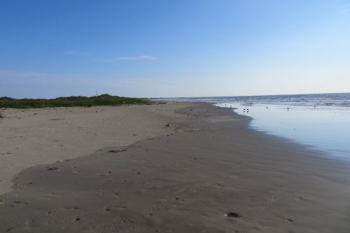 A serene beach scene with gentle waves, sandy shore, and a clear blue sky.