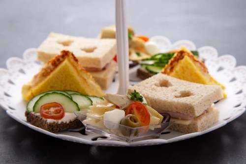 A tiered platter with assorted sandwiches, including cucumber, tomato, and a side of mixed vegetables.