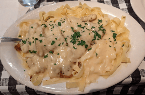 A plate of fettuccine pasta topped with creamy sauce and pieces of chicken, garnished with parsley.