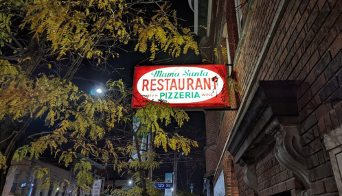 A brightly lit sign for "Mama Santa Restaurant & Pizzeria" hangs outside a brick building at night.