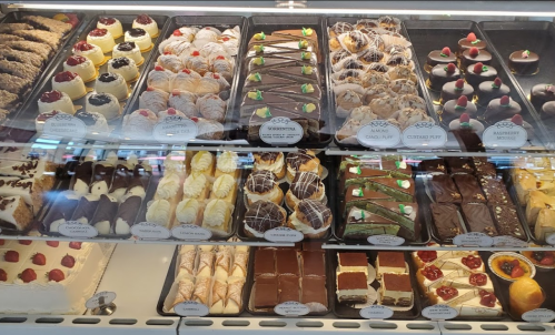 A display case filled with various colorful pastries and desserts, including cakes, tarts, and chocolate treats.