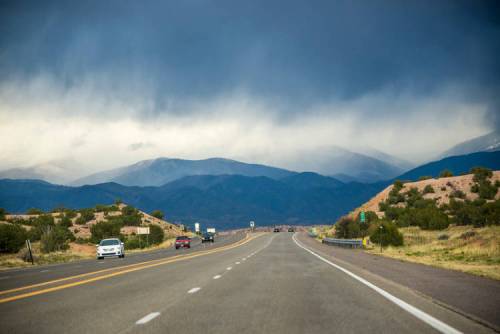 A scenic highway stretches into the distance, flanked by mountains and dark, cloudy skies.