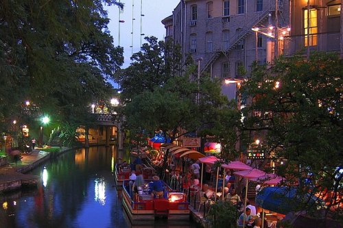 A scenic evening view of a canal lined with colorful boats and illuminated restaurants under a twilight sky.
