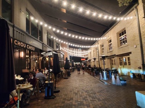 A cozy outdoor dining area with string lights, tables, and umbrellas, creating a warm evening atmosphere.