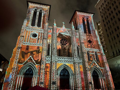 A historic church illuminated with colorful projections, showcasing intricate designs against a night sky.