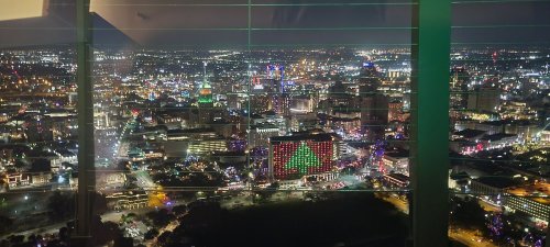 A panoramic night view of a city skyline adorned with colorful holiday lights and a large Christmas tree display.