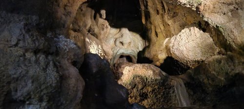 A cave interior with textured rock formations and a small waterfall, illuminated by soft light.