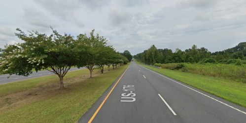 A wide, empty road lined with trees on one side, under a cloudy sky.