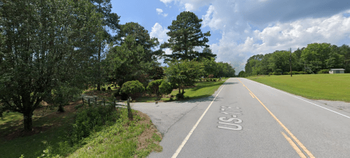A quiet rural road lined with trees and greenery under a partly cloudy sky.