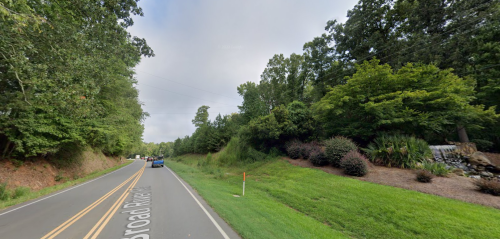A winding road lined with trees and greenery, with a few cars driving along the pavement.