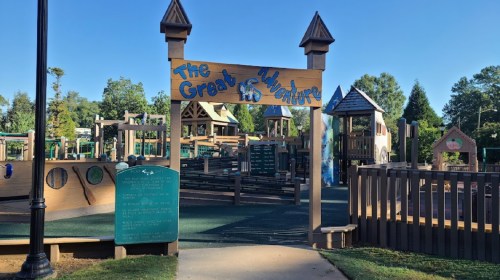 A colorful playground entrance sign reads "The Great Adventure," surrounded by play structures and greenery.