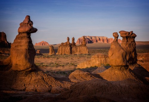 Unique rock formations rise from the desert landscape under a clear blue sky, showcasing natural sculptures at sunset.