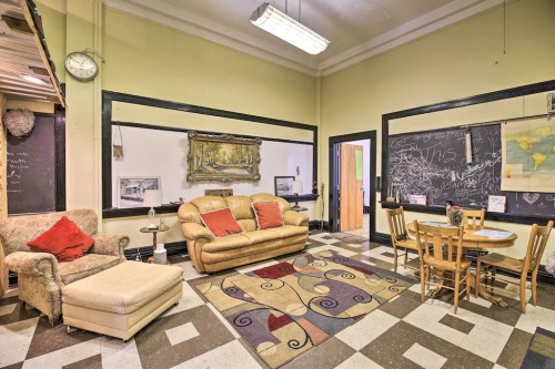 Cozy room with a sofa, armchair, dining table, and chalkboards, featuring a patterned rug and warm yellow walls.