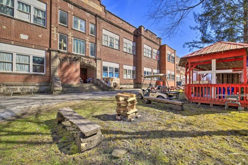 A brick school building with a gazebo and stacked logs in the foreground, under a clear blue sky.
