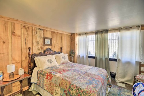 Cozy bedroom with wooden walls, a floral quilted bedspread, and large windows covered with sheer curtains.
