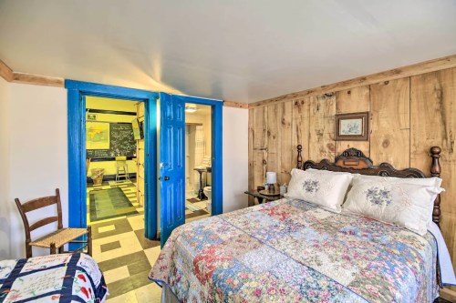 Cozy bedroom with a floral quilt, wooden walls, and bright blue doors leading to another room.