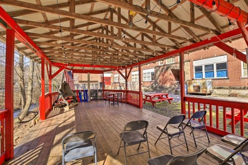 A spacious outdoor pavilion with wooden beams, red accents, picnic tables, and chairs, surrounded by trees and a building.