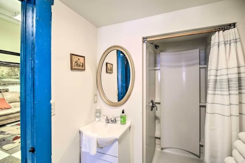 A bright bathroom featuring a round mirror, sink, and shower with a curtain, with blue door accents.