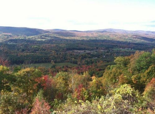 A scenic view of rolling hills and valleys, showcasing vibrant autumn foliage in various shades of red, orange, and green.