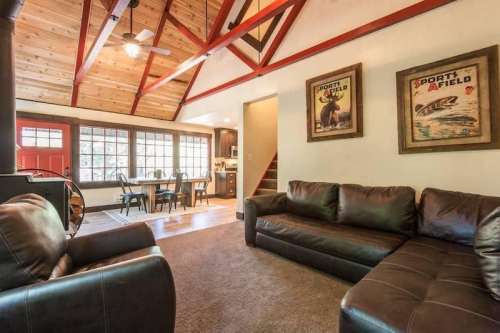 Cozy living room with leather sofas, wooden beams, and a dining area visible in the background. Warm, inviting atmosphere.