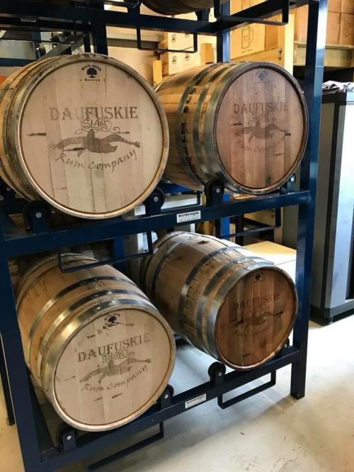 Three wooden barrels labeled "Daufuskie Rum Company" stacked on a metal rack in a storage area.