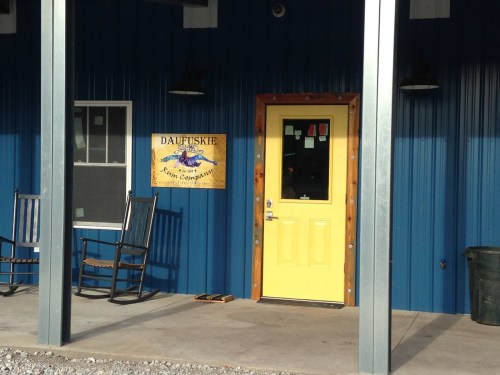 A blue building with a yellow door, rocking chairs on the porch, and a sign that reads "Daufuskie."