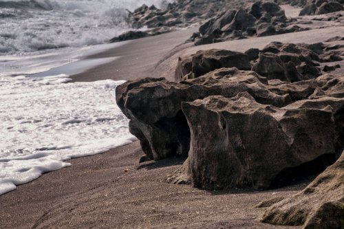 Rocky shoreline with waves gently lapping at the sand, creating a serene coastal scene.