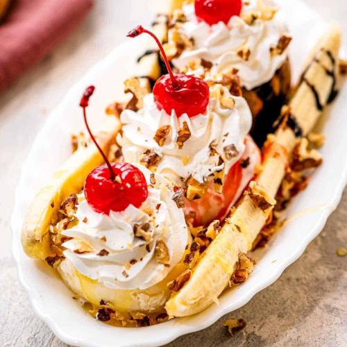 A banana split topped with whipped cream, cherries, and chopped nuts, served in a white dish.