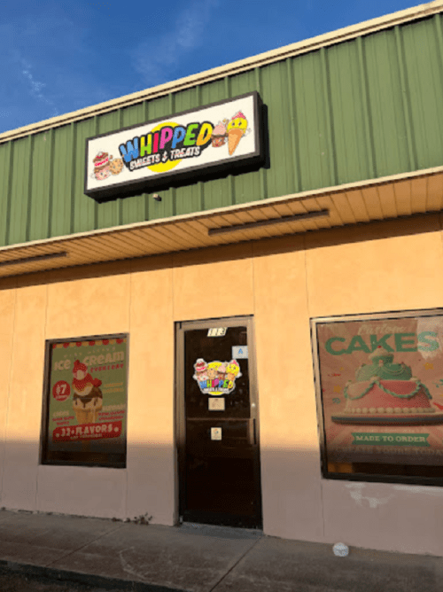 Exterior of "Whipped" bakery and treats shop, featuring colorful signage and large windows displaying desserts.