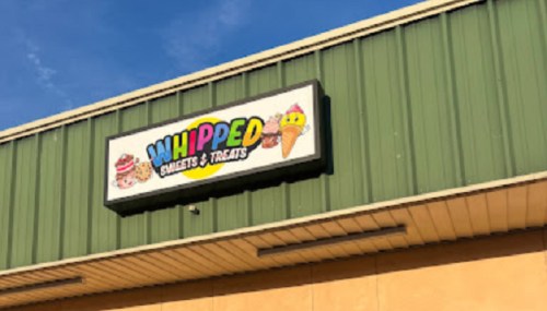Sign for "Whipped Sweets & Treats" featuring colorful graphics of desserts and ice cream against a green building.