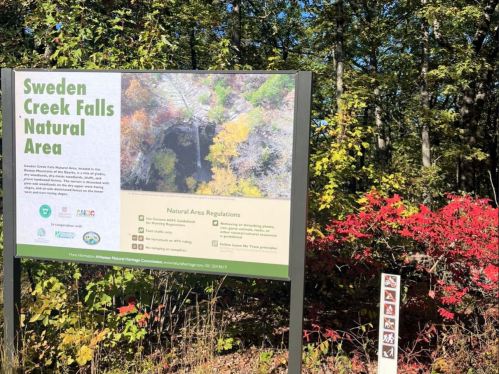Sign for Sweden Creek Falls Natural Area surrounded by trees and colorful autumn foliage.