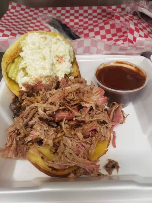 A pulled pork sandwich with coleslaw and pickles, served with a side of barbecue sauce.