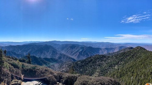 A panoramic view of rolling mountains under a clear blue sky, with lush greenery in the foreground.