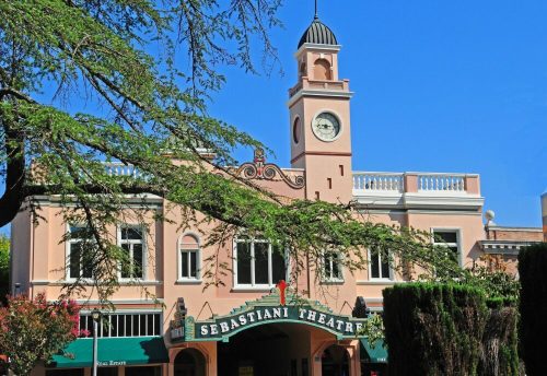 Historic Sebastiani Theatre with a clock tower, framed by trees and a clear blue sky.