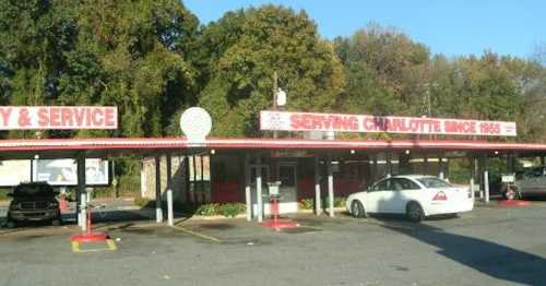 A retro drive-in restaurant with a red and white sign reading "Serving Charlotte Since 1955" and parked cars.