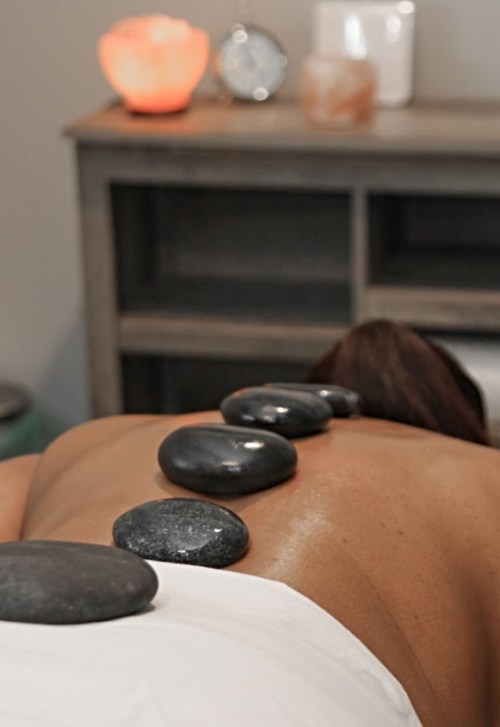 A person receiving a stone massage, with smooth stones placed along their back in a serene spa setting.