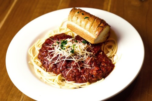 A plate of spaghetti topped with marinara sauce and grated cheese, served with a slice of garlic bread.