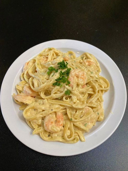 A plate of creamy shrimp fettuccine pasta garnished with parsley on a black table.