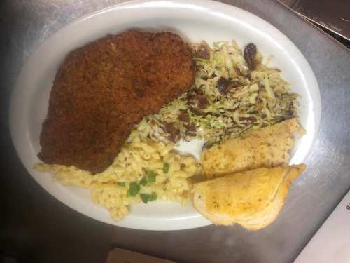 A plate of food featuring a breaded fried cutlet, macaroni and cheese, coleslaw, and two slices of garlic bread.