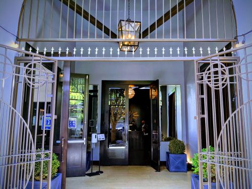 Entrance of a modern building with decorative gates, potted plants, and a chandelier visible inside.