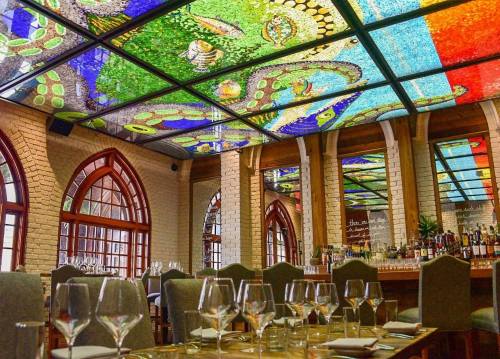 Interior of a restaurant featuring a colorful stained glass ceiling and elegantly set dining tables.