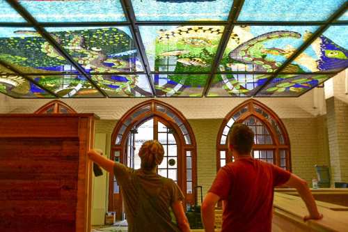 Two people admire a colorful, artistic glass ceiling featuring aquatic designs in a spacious interior.