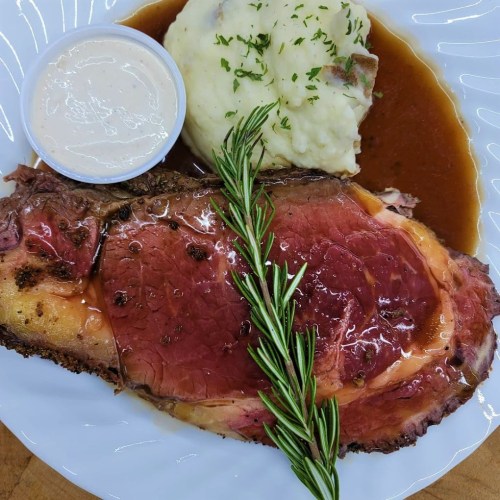 A plate featuring sliced roast beef, mashed potatoes, gravy, and a side of creamy sauce, garnished with rosemary.