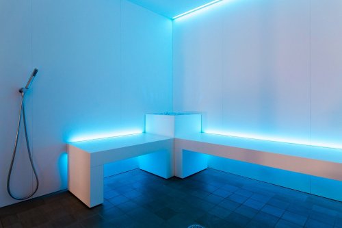 A modern, minimalist shower space with blue LED lighting and sleek white benches.