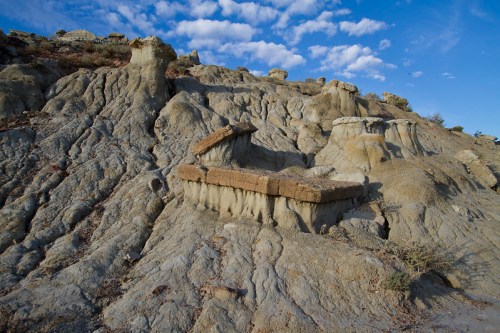 A rugged, rocky landscape with layered formations under a blue sky with scattered clouds.